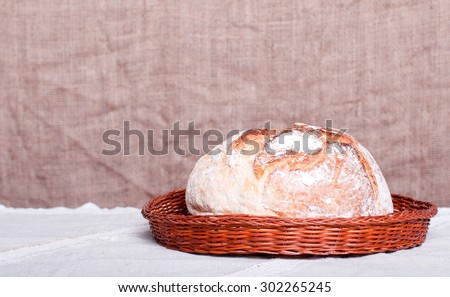 A loaf of round bread in a wicker basket on a bright tablecloth sacking in  background, side view