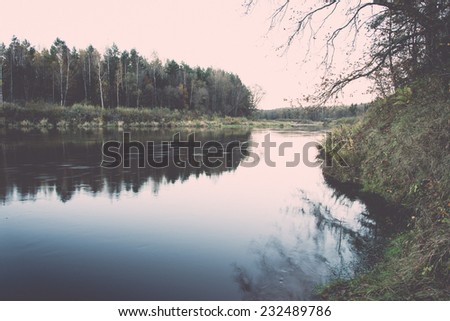 scenic autumn colored river in country with trees and reflections. Vintage photography effect.