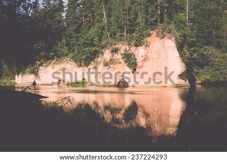 river with reflections in weater and sandstone cliffs in latvia - retro, vintage style look