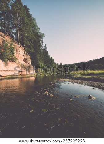 river with reflections in weater and sandstone cliffs in latvia - retro, vintage style look