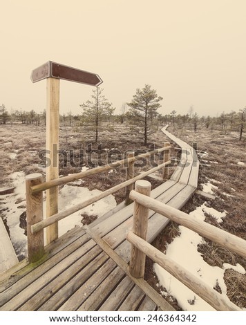 wooden boardwalk with empty direction sign and frozen nature - retro vintage effect