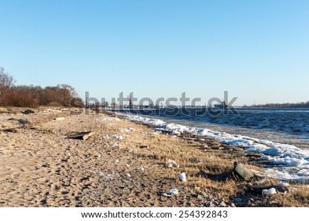 frozen beach near shipyard and sea port with rays of sun and wavebreaker