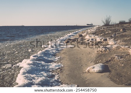 frozen beach near shipyard and sea port with rays of sun and wavebreaker - vintage retro grainy film effect