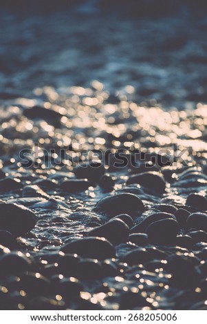 sun reflections on Stones on the beach and sea water in sunset light - retro vintage film effect