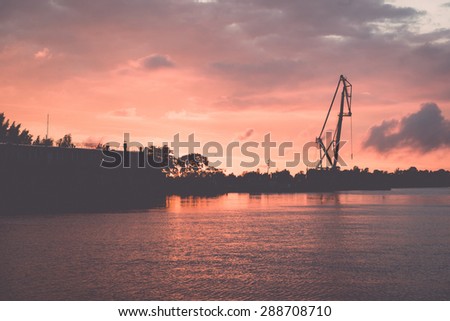reddish sunset over sea port with cranes in background - retro vintage film look