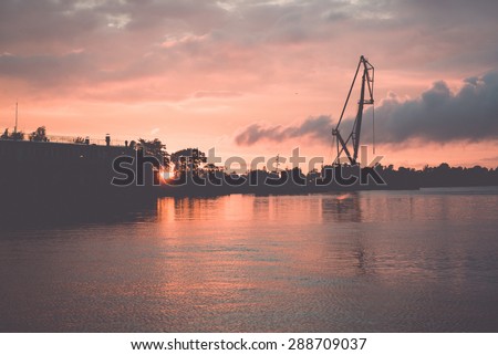 reddish sunset over sea port with cranes in background - retro vintage film look