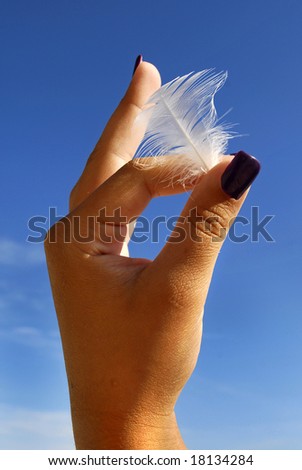 Woman's hand holding a feather against a blue sky