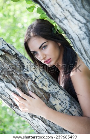 Girl with long hair peeking out from behind a tree