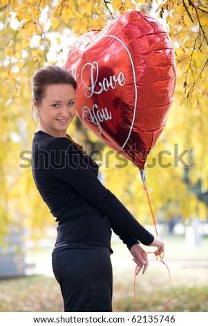 Young girl with a balloon in the form of heart on the background of yellow leaves.