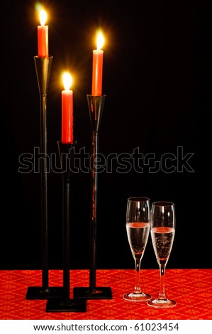 Three lit candles and two glasses of sparkling wine on a black background