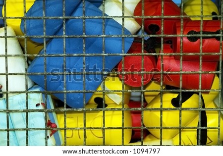 Colorful swim training aids and floats in a wire storage bin at poolside.