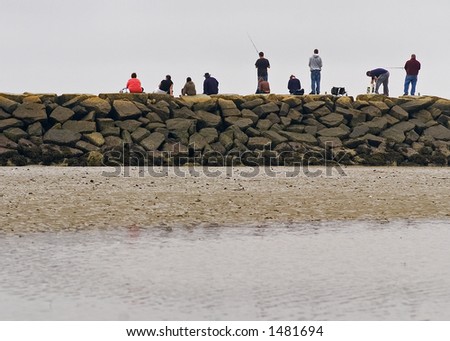 A line of people fishing from the breakwater in the Saco River in Biddeford Pool Maine.