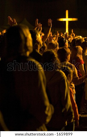 A crowd worships with illuminated cross