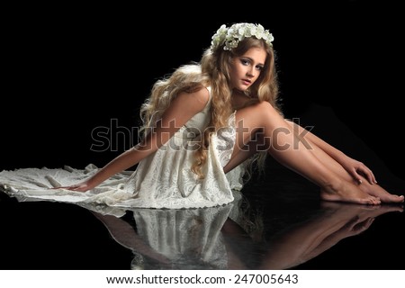 beautiful blonde girl with long hair. live orchids in hair. studio photo on a black background. model sitting on the floor