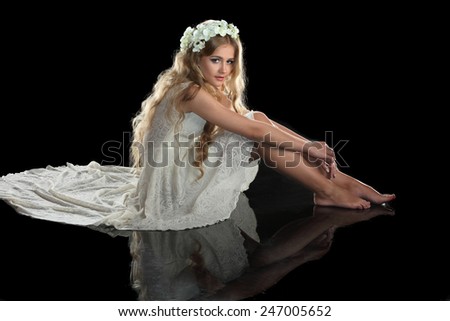 beautiful blonde girl with long hair. live orchids in hair. studio photo on a black background. model sitting on the floor