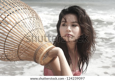 Pretty Asian woman with coop-like trap for catching fish in shallow water.