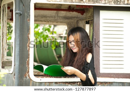 Asian woman reading at window of old train room .