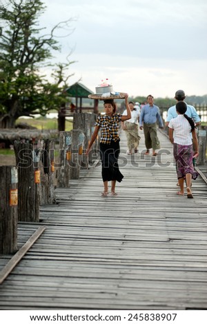 AMARAPURA,MYANMAR - JUNE 30 : Burmese woman carrying on her head walking on U Bein Bridge on June 30,2014,Amarapura in Myanmar.U Bein Bridge is the oldest and longest teak wooden bridge in the world.