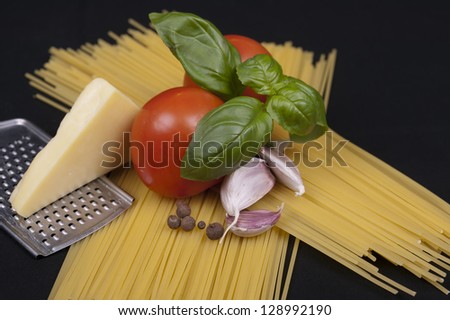 Spaghetti pasta, tomato, basil, garlic, black pepper and cheese isolated on a black background
