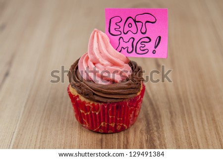 Vanilla cupcakes with pink frosting and eat me message on wood