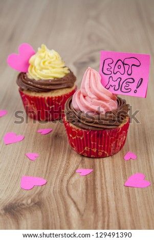 Vanilla cupcakes with pink hearts and eat me message on wood