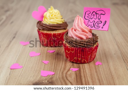 Vanilla cupcakes with pink hearts and eat me message on wood