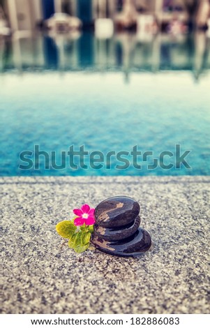 Zen massage black spa stones with pink flower near the pool