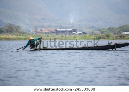 INLE LAKE, MYANMAR - FEBRUARY 15: Unidentified man rowing a wooden boat in Inle Lake with its leg-rowing and fishing. Intha people is a major tourist destination on Feb 15, 2014 in Inle lake, Myanmar.