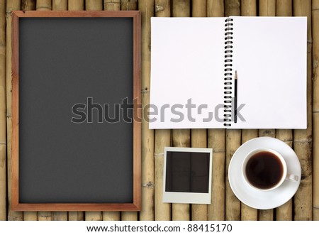 blank book and chalkboard with coffee cup and photo frame on bamboo background