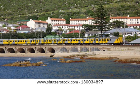 A commuter train passes Kalk Bay Harbour Beach on the scenic suburban line between Cape Town and Simonstown in South Africa.
