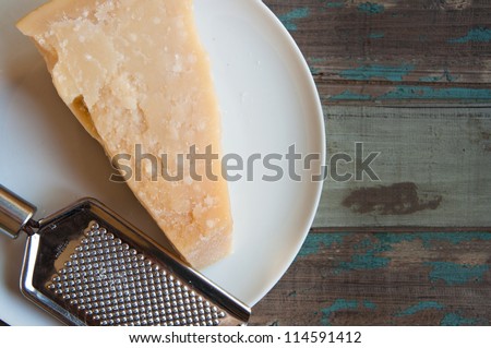 Traditional parmesan cheese on a white plate with a hand grater on a rustic wooden tabletop.