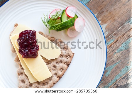 Swedish crisp bread topped with cheese and lingonberry jam and served with a side salad of cucumber, dill and radishes.