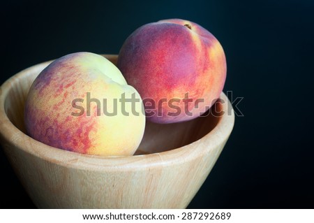 Fresh peaches served in a simple wooden fruit bowl isolated on a black background.