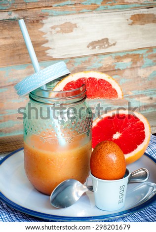 Healthy breakfast of a boiled egg, fruit smoothie and freshly cut grapefruit.Served against a rustic wood background.