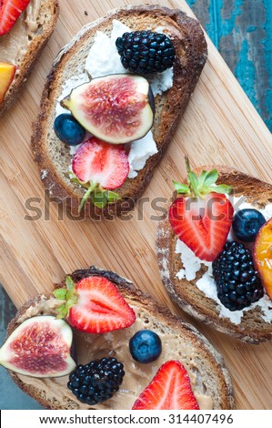 Healthy fruit topped open sandwich of Wholemeal rye bread with strawberry, blackberry, grilled peach and fig. Served on a wooden board.