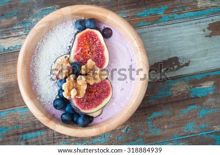 Healthy breakfast berry smoothie bowl of blueberry and strawberry blended with kefir yogurt and topped with fresh fig,blueberries,walnuts and coconut. Served in a wooden bowl on a rustic wooden table.