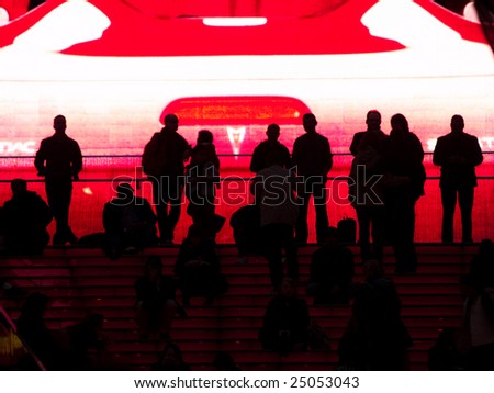 People silhouetted against huge video screen.