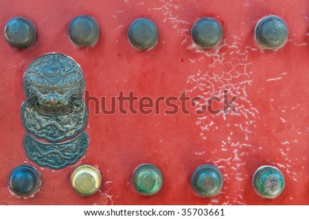 Traditional Black Chinese door knocker on a bright red aged door.