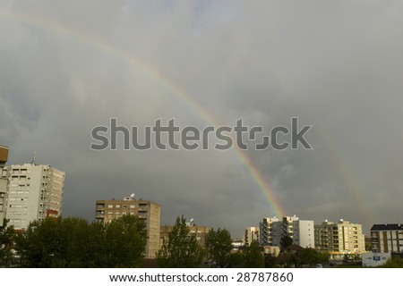 A rainbow on a cloudy sky rising between buildings