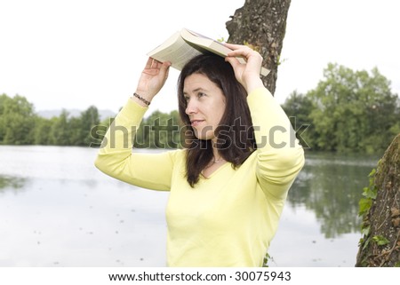 a young woman holding a book on her head protecting from the rain