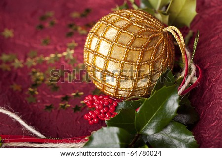 Christmas ball with a golden ribbon and  holly on red background and golden stars