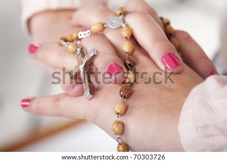 a young girl hands pray with a rosary