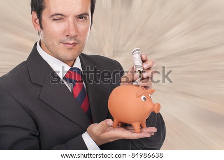 young businessman holding a piggy bank with dollar bills and blinking his eye