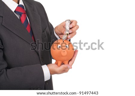 a young businessman holding a piggy bank and putting dollars inside