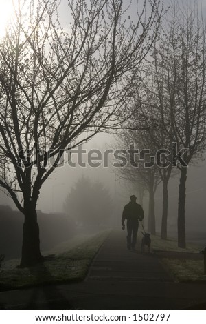 Man and dog on a morning stroll through the lifting fog.