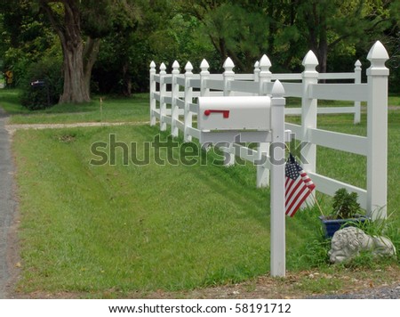 A white mailbox in front of a white fence with an American Flag
