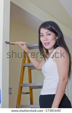 Asian Woman Contractor painting wall latter in background
