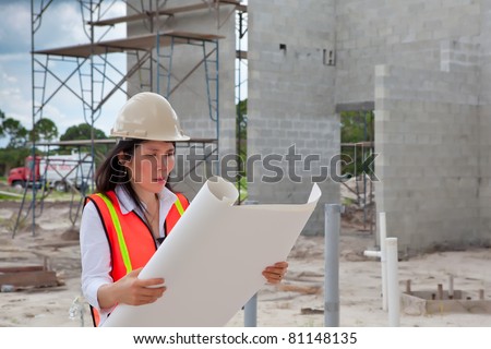 Asian Woman Inspector on construction site. Scaffolding, truck, plumbing pipes and  block walls in background.