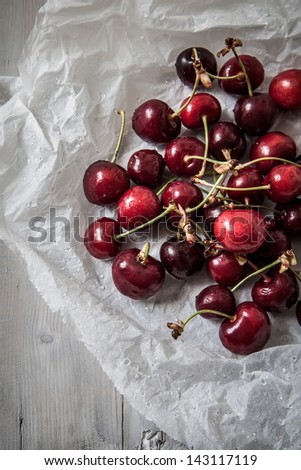 fresh sour cherries in paper with water drops on grey wooden table