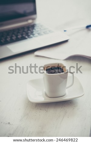 a coffeee cup on white table and laptop